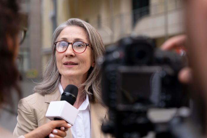 Mujer es entrevistada en exteriores por una reportera y cámara 