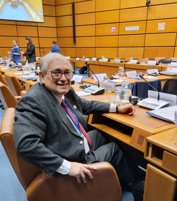 Humberto Piano, sentado en un salón con filas de asientos; hay micrófonos en cada lugar