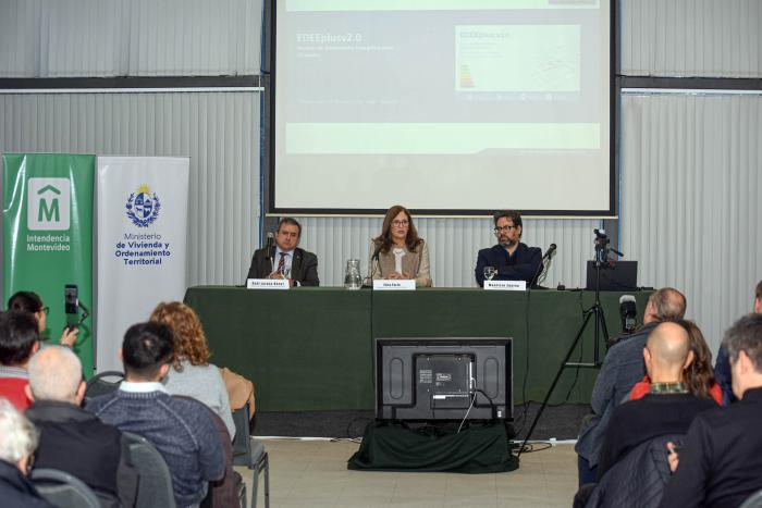 Al fondo; mesa de autoridades y un pantalla; más cerca, público, de espaldas