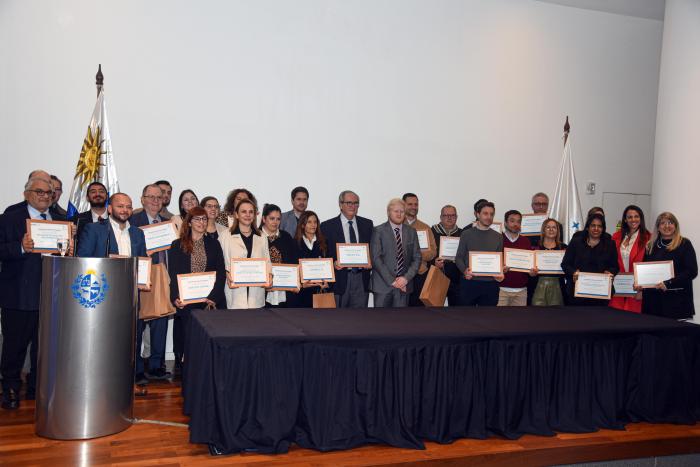 Todos los ganadores presentes, con diplomas, sobre un escenario con una mesa y un atril