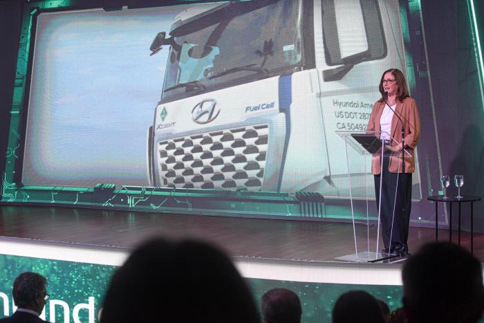 Ministra Elisa Facio Ministra habla en un escenario; detrás, pantalla con un camión; frente a ella, público
