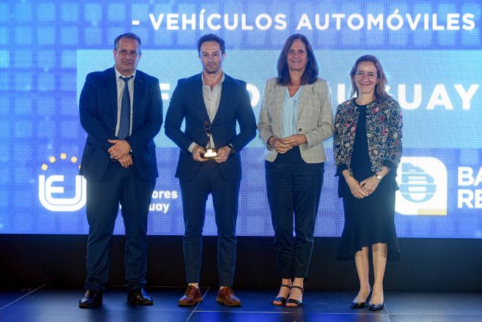 La ministra Facio, junto a dos hombres (uno sostiene un premio) y una mujer; detrás, una pantalla