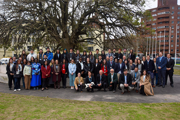 Foto oficial de las y los participantes Decenas de personas, de pie y en cuclillas, bajo un árbol