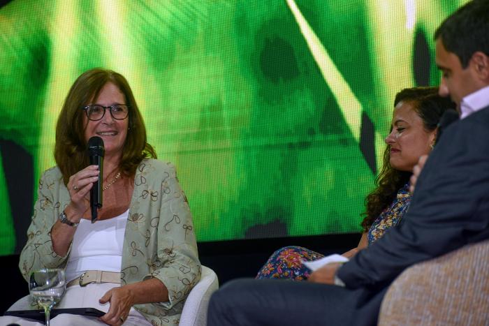 Ministra Facio habla, sentada; a su lado, una mujer y un hombre