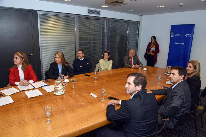 La firma de convenio se realizó en la Torre Ejecutiva Integrantes de las instituciones están sentados en una larga mesa; al fondo, banner de AUCI