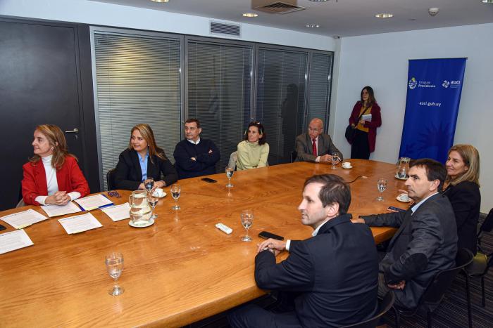 Integrantes de las instituciones están sentados en una larga mesa; al fondo, banner de AUCI