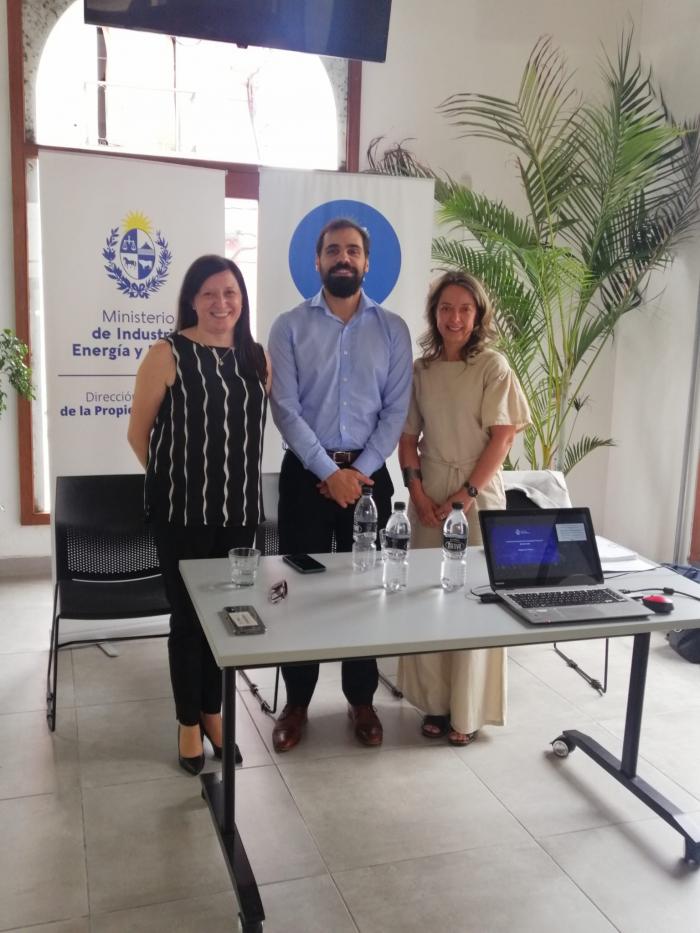 Imagen de los representantes de MIEM-DNPI en el taller desarrollado en Rocha Un hombre y dos mujeres posan detrás de una mesa; a la vez, detrás de ellos hay dos banners