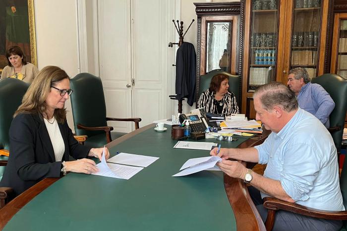 Ministra e intendente firman documentos en una sala con muebles y otras personas
