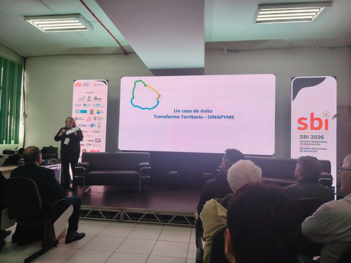 Directora Ximena Cidrás en la Semana Binacional de la Innovación Directora Cidrás, de pie; detrás, cartelería; más cerca, público