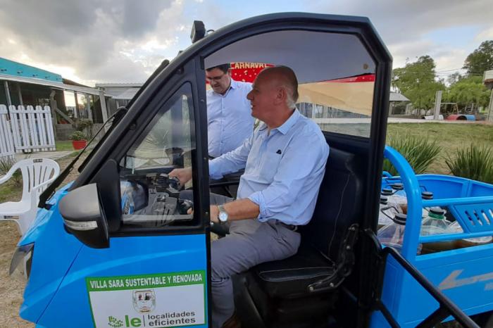 Verri en un triciclo eléctrico celeste; a su lado, afuera, está el director Fitzgerald Cantero