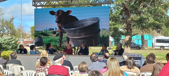 Asistentes ven un audiovisual en que aparece una vaca; están sentados al aire libre