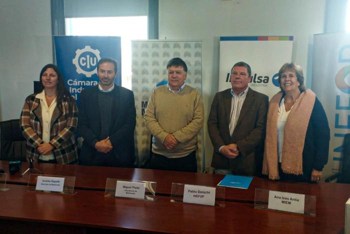 Dos mujeres y tres hombres posan, de pie, detrás a una mesa; a su vez, detrás de ellos hay banners