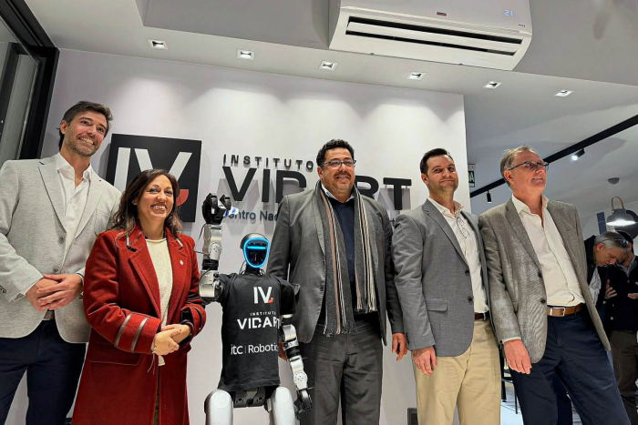Autoridades, de pie. Entre ellas, robot con el logo del Instituto Vidart. Detrás, pared con el logo 