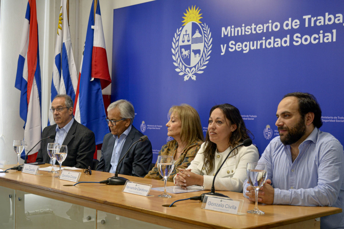 Cinco autoridades, sentadas en una mesa; detrás, banderas y banner del MTSS