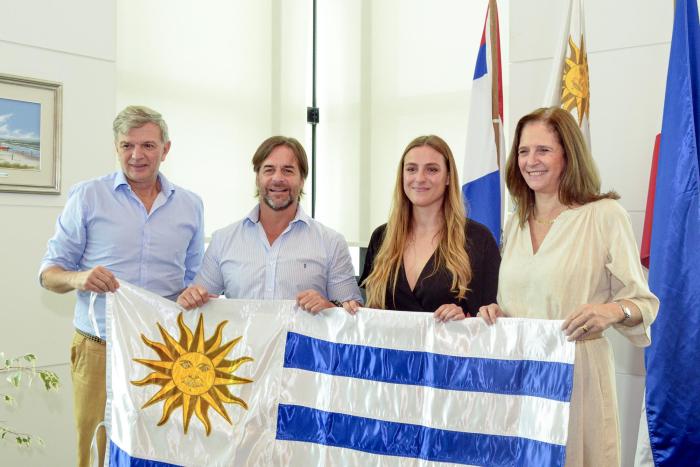 Entrega del pabellón nacional a la piloto Patricia Pita Lacalle Pou, Facio, Bauzá y Pita sostienen el pabellón nacional; detrás se ven pabellones patrios