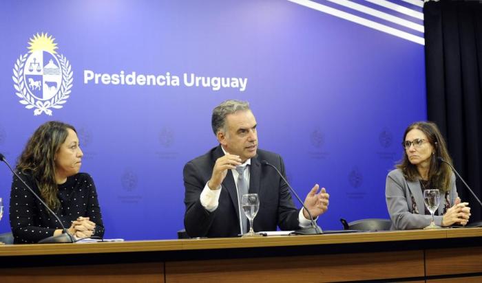 Presidente Orsi, habla frente a micrófono. Junto a él, ministra Cardona y Cecilia San Román.