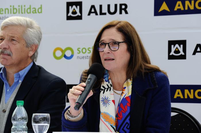 Ministra Facio habla, junto a un hombre, en la mesa de autoridades; detrás, banner de ALUR