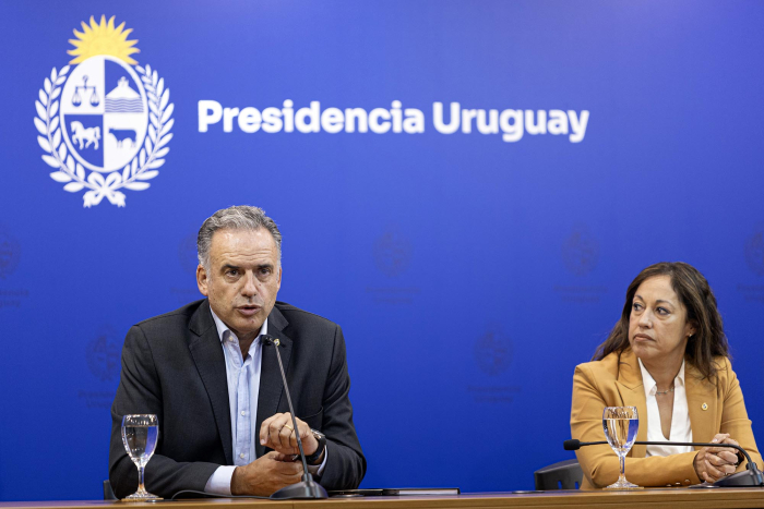 Orsi y Cardona, sentados; detrás, banner de Presidencia de la República