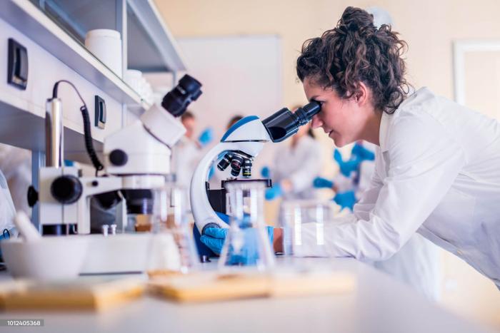 Una mujer vestida de túnica mira a través de un microscopio
