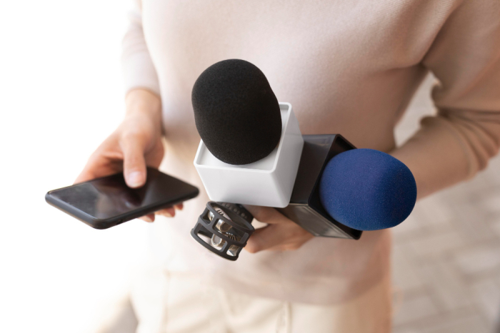 Mujer periodista sostiene entre sus manos micrófonos, grabadora y celular 