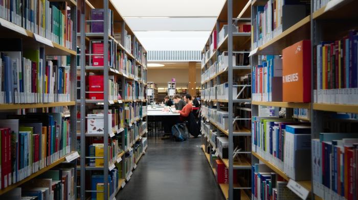 Vista de un salón de biblioteca, con estantes de libros y escritorios ocupados