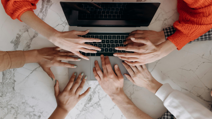 Muchas manos trabajan sobre una computadora 