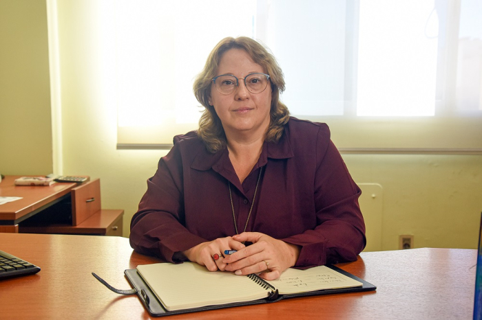 Ximena Cidrás sentada detrás de escritorio de madera. Sus manos están sobre un cuaderno abierto. 