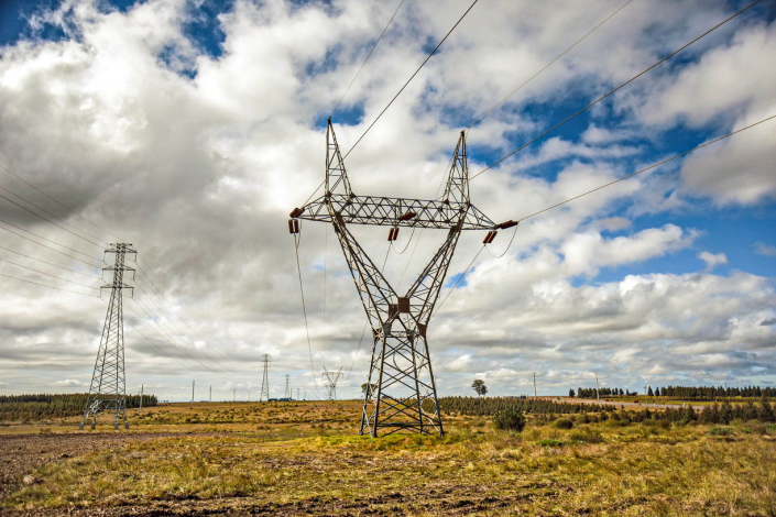 Torre eléctrica en el campo, bajo un cielo con nubes