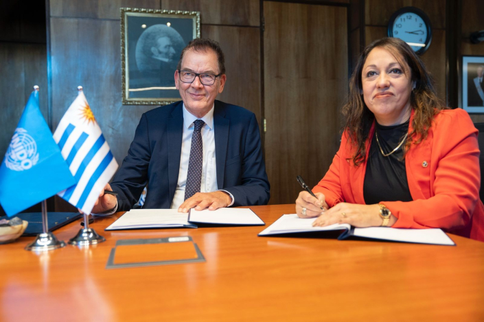Müller y Cardona, sentados, con documentos y banderas de Uruguay y de ONUDI