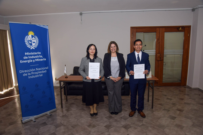Tres personas paradas junto a un banner institucional 