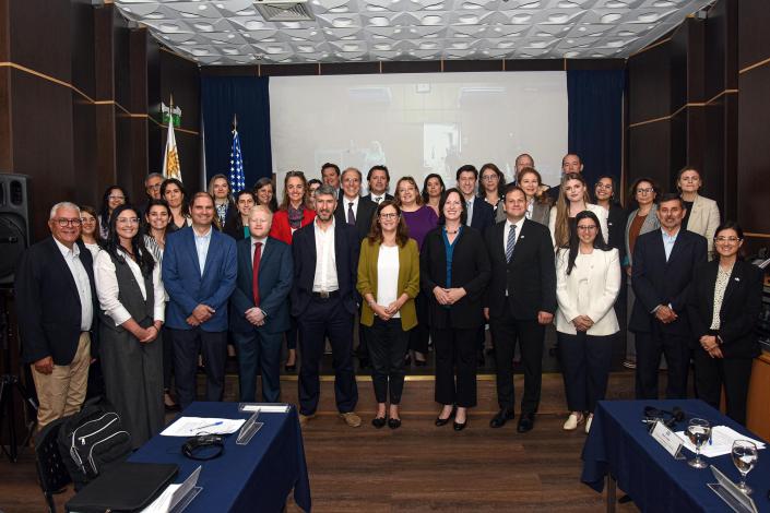 Participantes, de pie; detrás, pantalla y bandera