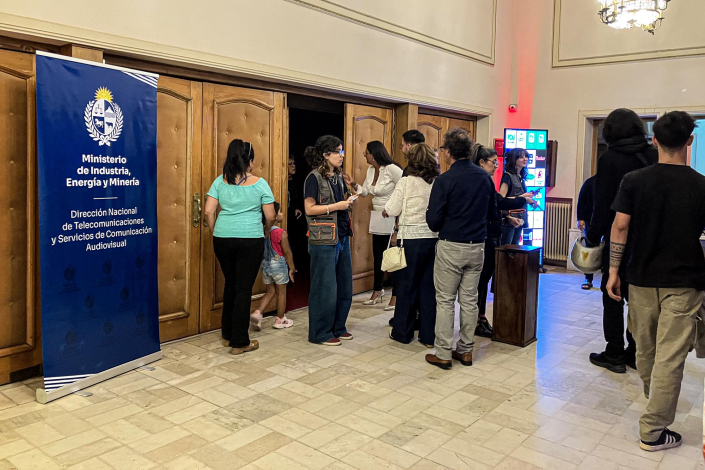 Personas en el hall del teatro; hay un banner del MIEM