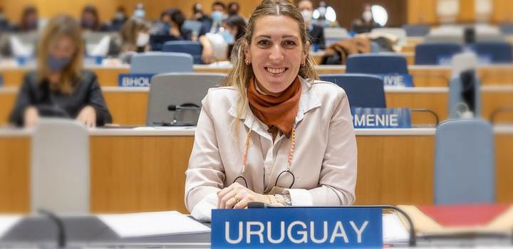 La directora Estrada durante la asamblea; detrás se ven otras personas y delante el cartel "Urguuay"