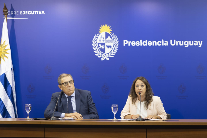 Ministra Cardona y ministro Oddone sentados. Detrás, fondo azul con logo de Presidencia y bandera. 