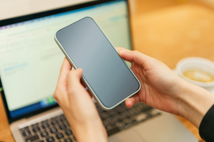 Manos que toman celular frente a una computadora