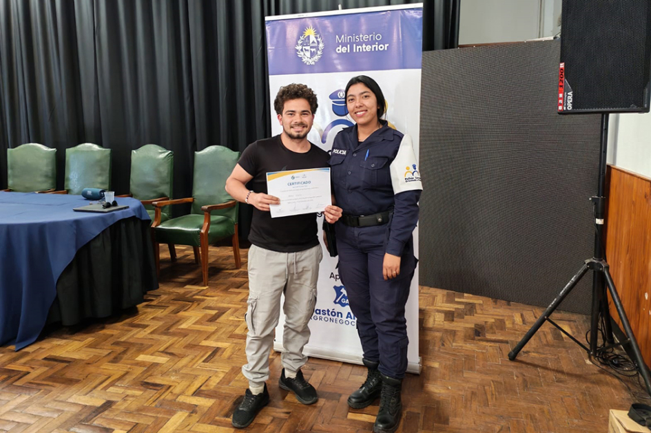Agente Maria Lauda Da Rosa entregando certificado a participante en Escuela de Seguridad Ciudadana