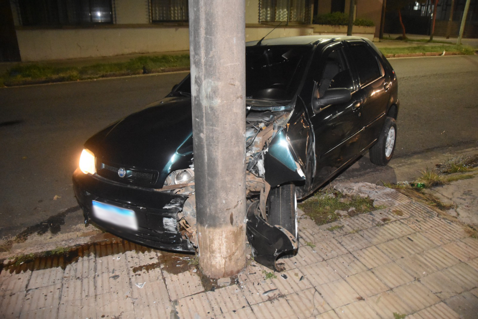 Automóvil negro incrustado contra una columna de hormigón, con importantes daños.