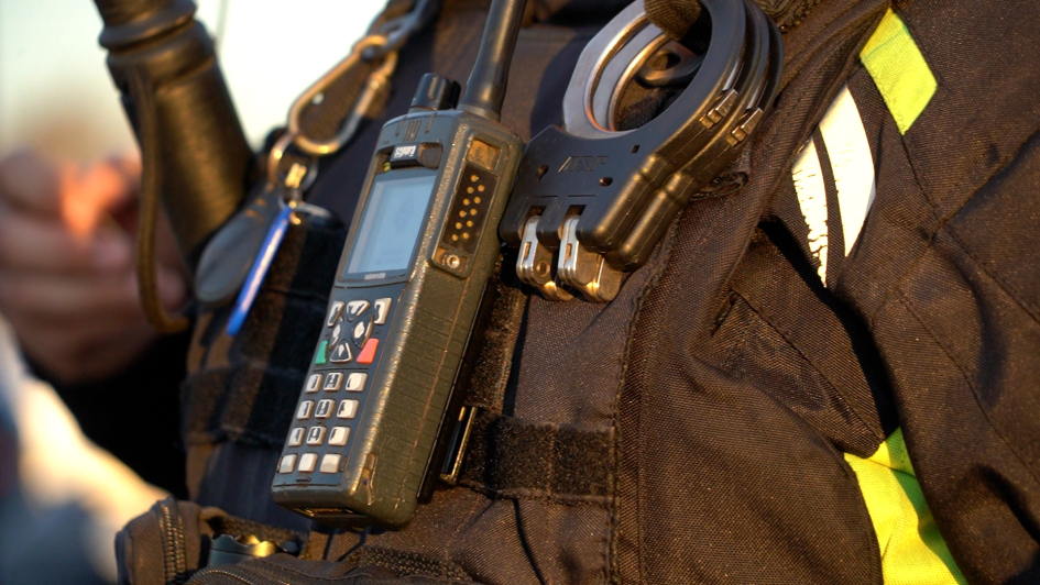 Equipamiento policial utilizado en tareas de prevención, patrullaje y respuesta ante incidentes Primer plano de radio portátil y esposas sujetas al chaleco de un funcionario policial activo.