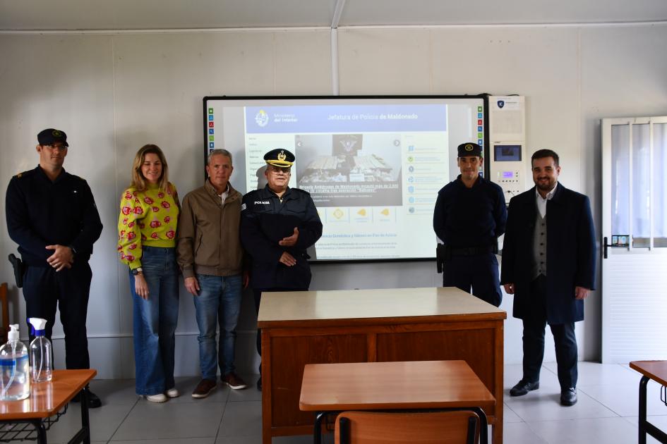 seis personas paradas posando junto a una pantalla, que fue donada a la Escuela de Policía