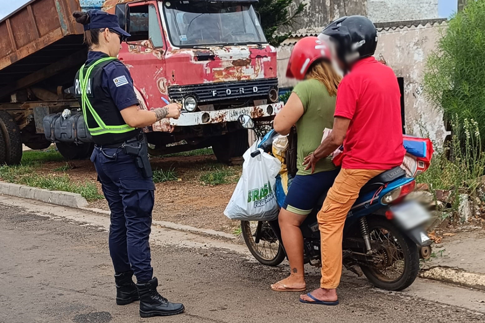 Dos personas en moto siendo inspeccionadas por una policía.