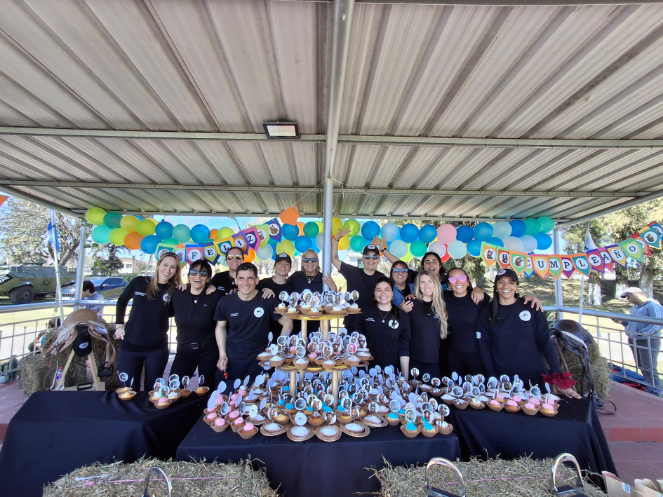 Integrantes sonriendo tras una mesa llena de cupcakes, globos y un cartel de feliz cumpleaños.