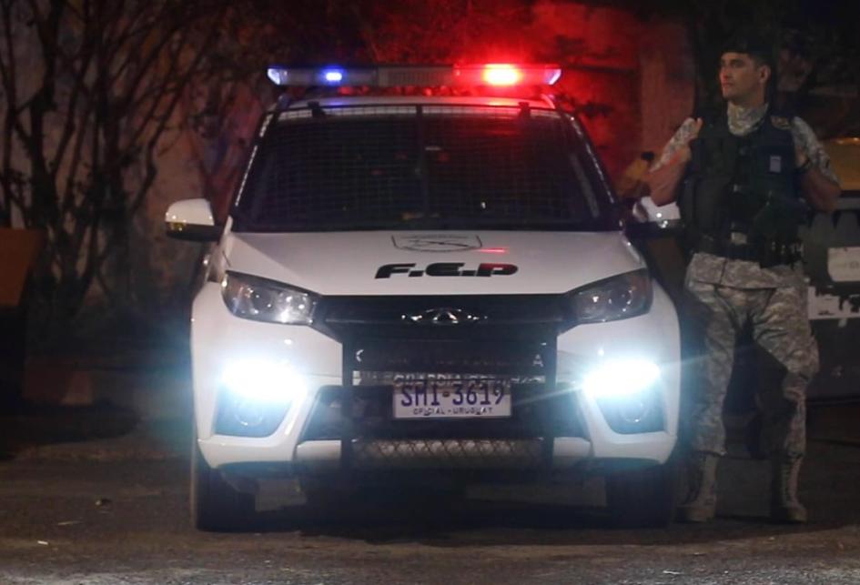 una camioneta policial estacionada con las luces encendidas y un policía parado al costado