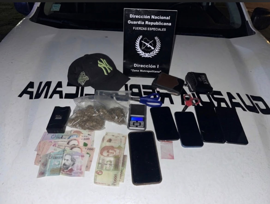 Objetos incautados: billetes, celulares, drogas, gorra y balanza junto a cartel de la DNGR