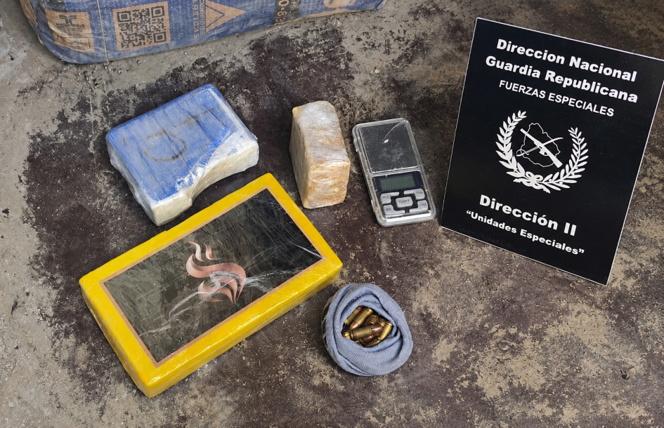 Tres ladrillos de droga, balanza de precisión, municiones y cartel policial en un piso