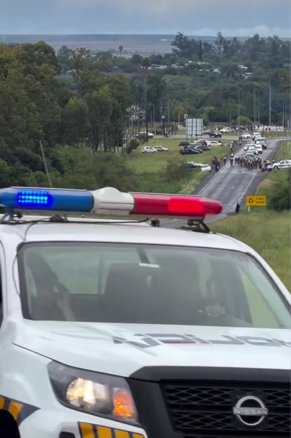 Movil policial en ruta con ciclistas de fondo.