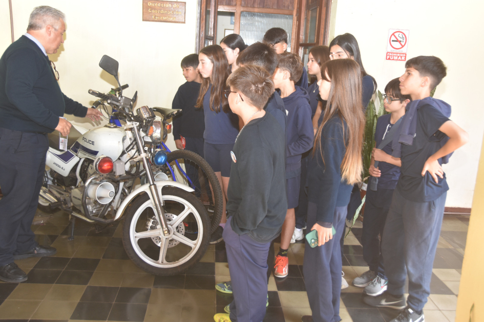 Niños escuchando atentos a un funcionario policial informando sobre el funcionamiemto de una moto