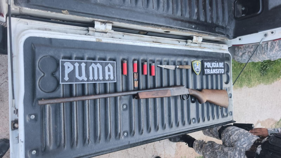 Escopeta, cartuchos y cuchillo incautados sobre la caja de una camioneta policial.