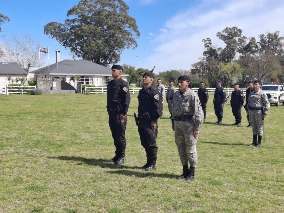 Policias destacados en la ceremonia Tres efectivos policiales alineados de pie sobre el pasto, dos de uniforme negro y una de pixeleado