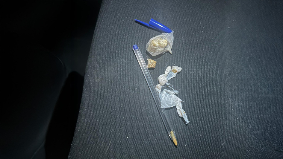 Bolsa y envoltorios con pequeñas piedras amarillentas junto a un bolígrafo sobre un asiento oscuro