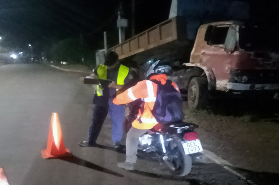 Un hombre en moto siendo controlado por un policía con un camion estacionado al fondo.
